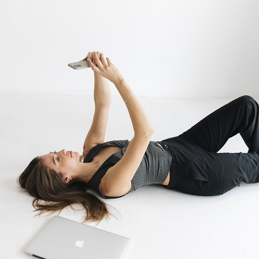 Girl laying in studio looking at phone on photo editing apps with macbook next to her for Wolfe Creative, a social media marketing agency